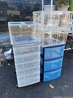 Photo of the entire lot showing stacked clear plastic storage bins on top of a blue storage bin and a white rolling mini chest next to them.