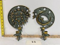 Full view of both sun and moon brass candle sconces side by side against white background with measuring tape for scale.