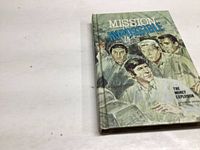 Photo of the front cover of the 1970 Mission Impossible book showing vintage illustrated art of characters and book title.