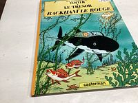 Photo of the front cover of the comic book 'Le Tresor de Rackham le Rouge' showing Tintin underwater with a submarine and sea creatures