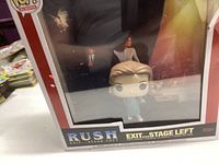 Side view of the Funko Pop box showing the character in light blue clothing with figure title on bottom right corner as Exit Stage Left and Rush logo. Reflective surface shows some background items.