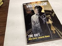 Paperback graphic novel titled 'Constantine Hellblazer The Gift' by Mike Carey and Leonardo Manco on a white surface.