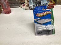 Unopened Hot Wheels 2012 Star Trek USS Enterprise packaged miniature starship on a display stand with blue and white branding packaging.