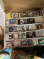 Photo showing multiple rows of baseball cards stacked neatly inside a large white box, cards featuring various players and designs.