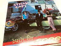 Front album cover of Stray Cats "Built For Speed" showing band members and classic cars.