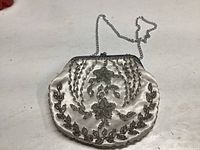 Vintage off-white satin beaded purse with silver floral and leaf bead embellishments and silver metal chain strap lying flat on a white surface.