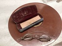 Overall view of the vintage spectacles and their leather case on a surface.