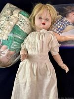 Composite doll with blonde hair wearing white lace dress, closed eyes, and worn paint.