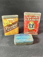 Overview of three antique tobacco tins: Union Leader, Picobac, and Edgeworth, showing condition and label details