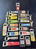 Photo showing most of the 25 vintage beer bottle openers arranged flat, displaying various brand names and colors.