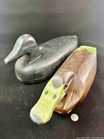 Photo of two carved wooden duck decoys, one black and one brown with green and white paint, showing front angle and paint wear.
