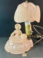 Front view of the vintage pink Jeannette glass lady lamp with frosted translucent pink shade and seated lady figure base near electrical cord and switch.