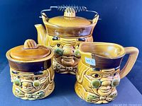 3-piece tea set with brown glaze and caricatured faces resembling Benjamin Franklin against dark background