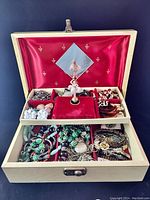 Open view of jewelry box showing ballerina figure on red velvet platform and compartments filled with assorted costume jewelry including earrings, bracelets, and pendants.