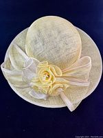 Full view of one light beige summer hat showing wide brim with decorative mesh bow and three mesh flowers.