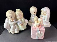 Front view of all three Precious Moments figurines: engagement scene, wedding couple, and pink keepsake box with bride and groom topper