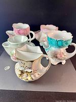 Six vintage porcelain shaving mugs and moustache cups arranged on a black surface, showing variety in colors and floral decorations.