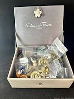 Closed box with floral knob, labeled Oscar de la Renta Parfums filled with individually bagged earrings