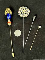 Four vintage hat pins laid out on black background with a quarter for size reference.
