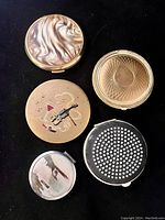 Overview of 5 vintage ladies compacts with different designs on a black background.