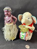 Front view of both vintage windup toys: Hawaiian hula girl and musical elephant next to a quarter for scale