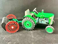 Green Kovap Zetor tin toy tractor with rear rake attachment, side view showing detailed painted engine and wheels.