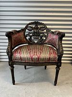 Front view of antique carved chair showing upholstered seat and armrests with carved details.