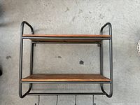 Front view of the coat rack showing two wooden shelves set within a black metal frame.