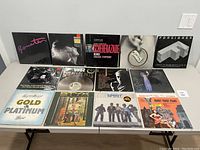 Front view of the vinyl record album covers arranged in two rows on a white table, showing full cover artwork of 13 records including Pat Benatar, Tears for Fears, Chicago Symphony, Golden Earring, Foreigner, Don Henley, War, John Barry, Stevie Nicks, Lynyrd Skynyrd, Styx, Spirit, and Pete Handy.