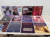 Top view of vinyl album covers arranged in two rows, shows all 12 album covers in the lot, including colorful artwork and artist names.