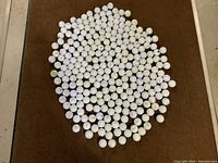 Top-down view of over 250 used, cleaned golf balls laid out on a dark surface showing the quantity and condition.