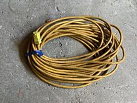 Coiled yellow heavy duty extension cord on concrete floor showing plug and outlet ends.