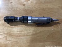 Side view of the Campbell Hausfeld air ratchet showing the whole tool on a wood surface.