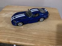 Side angle of blue Dodge Viper diecast car with white racing stripes on a wooden surface.