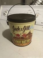 Front view of vintage Jack & Jill Peanut Butter tin bucket showing colorful graphics, brand name, and metal handle.