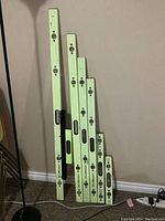 Full view of six aluminum levels vertically arranged by size against a beige wall and carpeted floor.