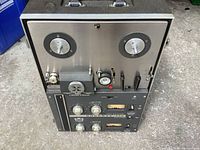 Front view showing empty reel spindles, control knobs, meters, and buttons on a rectangular recorder unit.