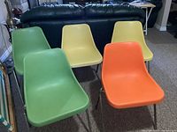 Front view showing five molded shell chairs in varying colors (yellow, green, orange) with metal legs arranged on carpet in a living room.
