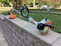 Full view of STIHL trimmer resting on stone wall, showing engine, shaft, loop handle, cutting guard.
