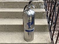 Front view photo showing the full body of the bright silver extinguisher with a blue and white label and pull pin.