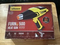 Box of Wagner Furno 500 heat gun showing product image, brand, and features including 12 settings, 1500 watts, LED controls, temperature range 100°F to 1200°F, and two included nozzles.