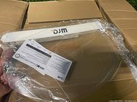 Photo showing multiple disposable face shields stacked in a box, individually wrapped in plastic with a white headband labeled 'DJM' and clear curved visor.