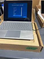 Laptop open showing Windows setup language selection screen and keyboard, placed on cardboard box