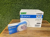 Box and individual glove package showing Elara Prepfit Medium vinyl gloves branding, with 100 count per box, latex free and powder free marked.