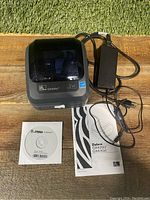 Printer with power adapter, installation CD, and user manual displayed on wood surface