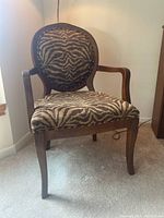Front view of wooden frame armchair with zebra print upholstery placed on carpeted floor.