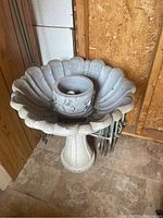 Overall view of the concrete bird bath next to a stack of metal garden edgers in a shed corner.