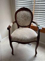 Front view of wood framed upholstered chair showing carved detail at top of backrest and patterned beige fabric seat and back.