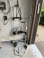 Photo of two folding dollies standing with metal frames and black handles, gray folding base platform, and wheels on a garage floor.