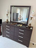 Front view of dark brown six-drawer dresser topped with matching rectangular mirror; decorative items on surface.